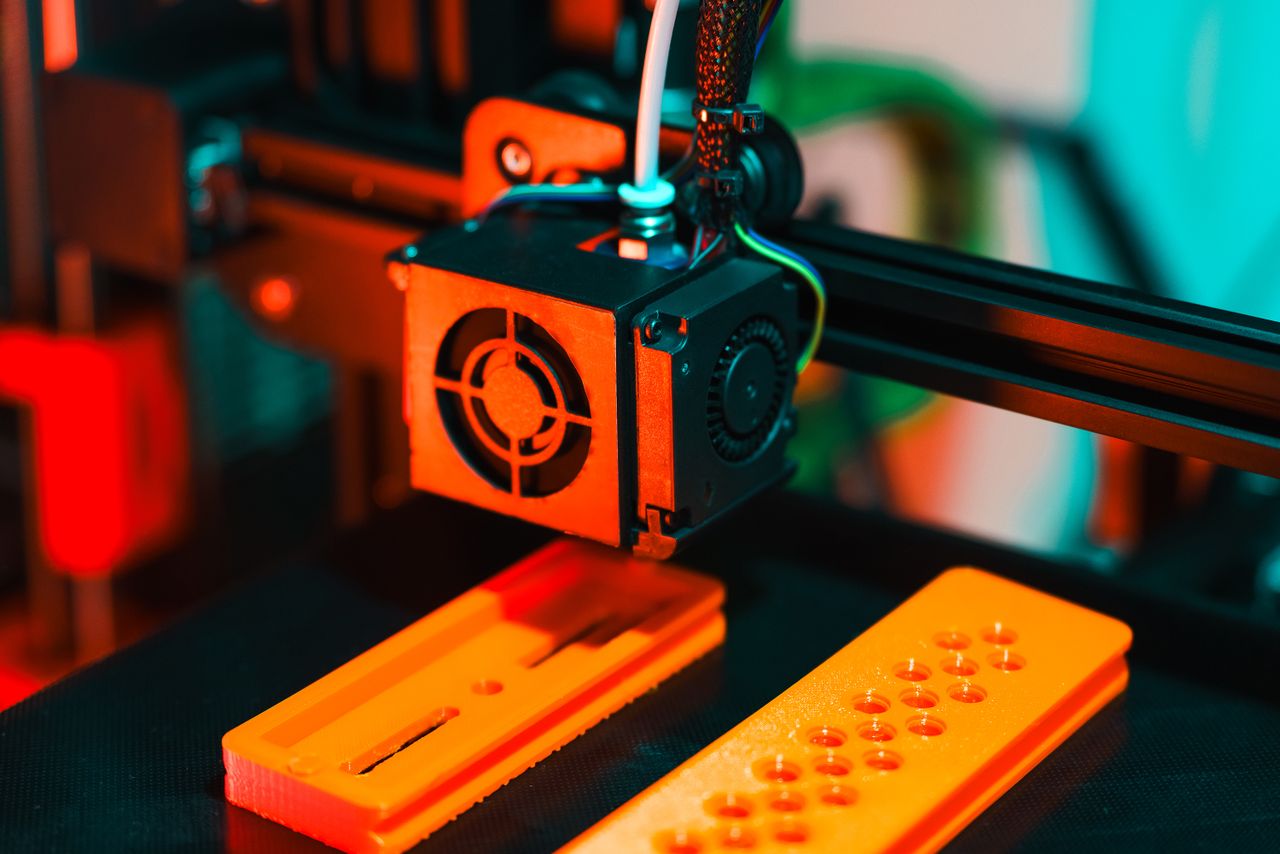 Services Detailed view of a 3D printer in action, extruding orange plastic components.