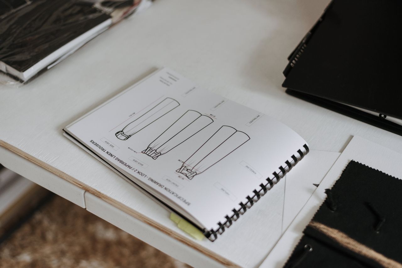 About From above of sketchbook with sketches of new collection of clothes placed on white table in modern light professional studio with various folders